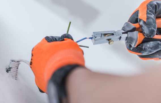 Electrician snipping wires with a pair of pliers and wearing electricial safety gloves